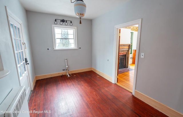 unfurnished room with a brick fireplace, radiator, and dark hardwood / wood-style floors