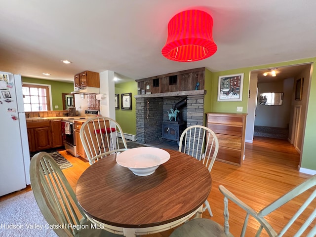 dining area with light wood-type flooring, a wood stove, sink, and baseboard heating