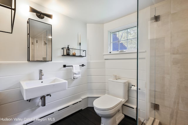 bathroom featuring a baseboard radiator, toilet, a shower with door, and sink