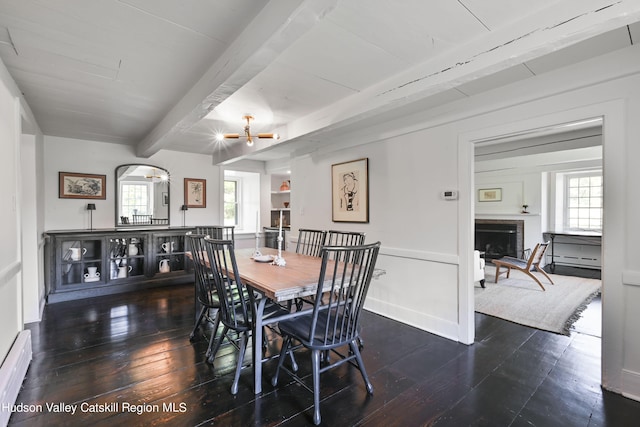 dining room featuring beamed ceiling, a baseboard heating unit, plenty of natural light, and dark wood-type flooring