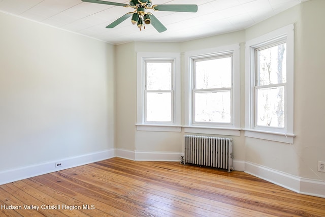 empty room with a healthy amount of sunlight, radiator heating unit, ceiling fan, and light hardwood / wood-style flooring