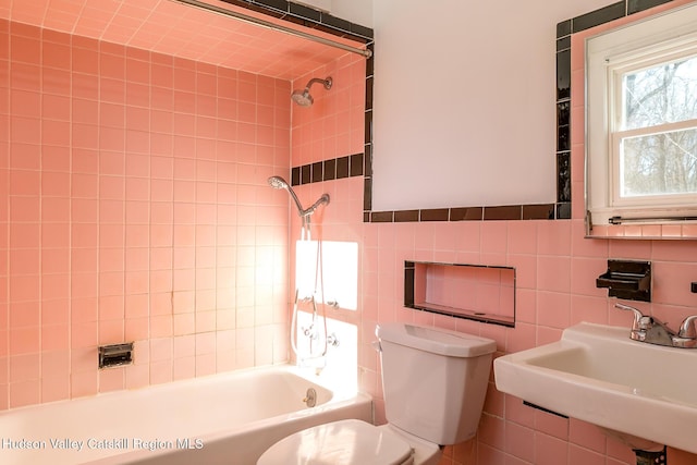 full bathroom featuring tiled shower / bath, toilet, sink, and tile walls