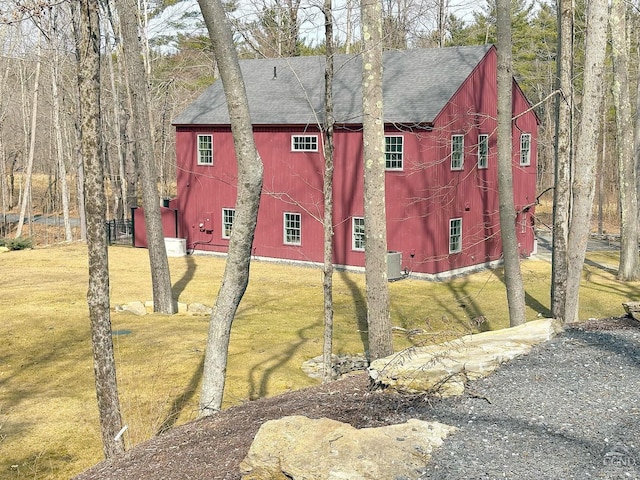  - view of property exterior featuring a shingled roof, a lawn, central air condition unit, and a barn