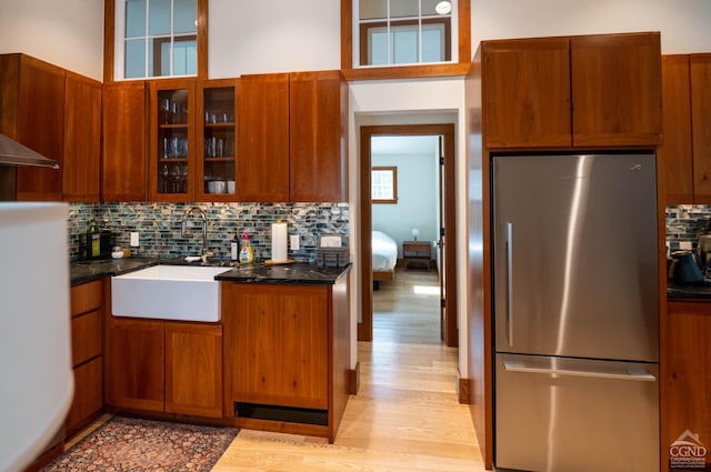  - kitchen with freestanding refrigerator, a sink, light wood-style floors, tasteful backsplash, and glass insert cabinets