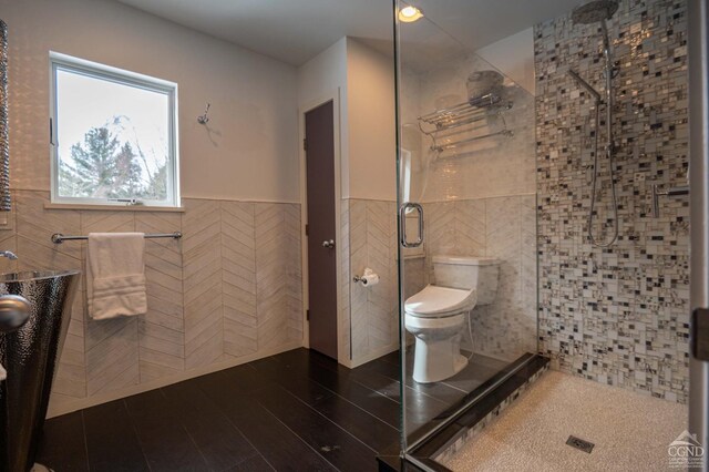  - full bathroom with tile walls, a shower stall, toilet, a wainscoted wall, and wood finished floors