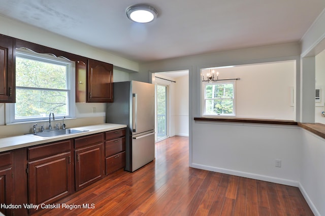 kitchen with dark wood-type flooring, an inviting chandelier, sink, stainless steel fridge, and dark brown cabinets