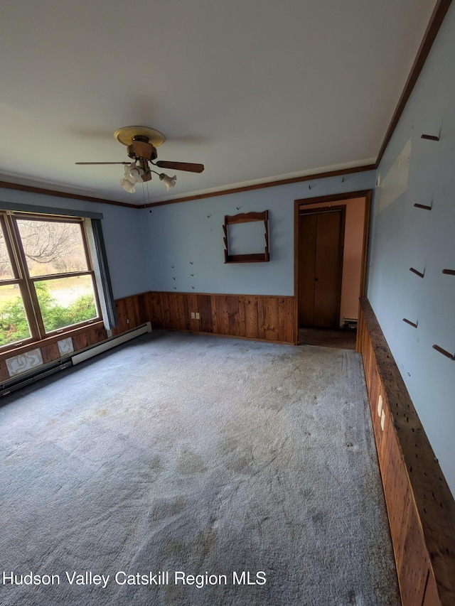 carpeted empty room featuring ceiling fan, wood walls, ornamental molding, and baseboard heating