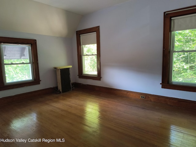 unfurnished living room with a wealth of natural light, hardwood / wood-style flooring, vaulted ceiling, and radiator