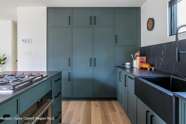 kitchen featuring backsplash, dark countertops, appliances with stainless steel finishes, a sink, and light wood-style floors