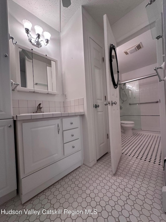 full bathroom with toilet, a textured ceiling, decorative backsplash, shower / bath combination with glass door, and vanity