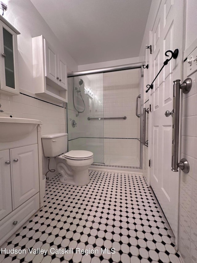 bathroom featuring vanity, a shower with shower door, tile walls, and toilet