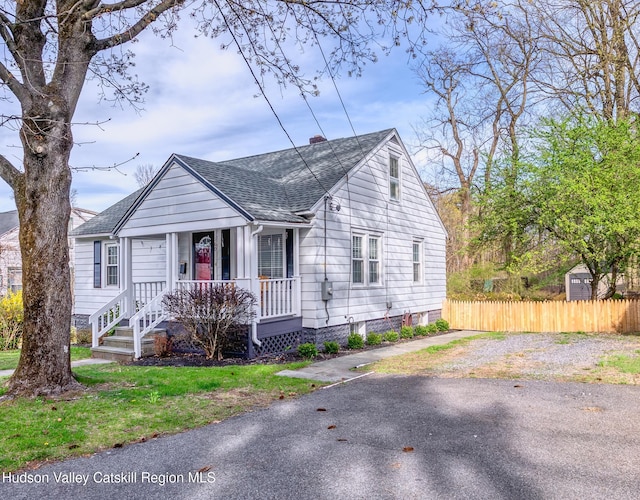 bungalow-style home with roof with shingles, a porch, a chimney, and fence