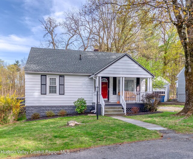 view of front facade featuring a chimney, roof with shingles, a porch, and a front yard