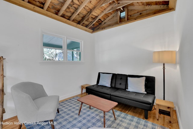 living area with baseboards, lofted ceiling with beams, wood ceiling, and wood finished floors