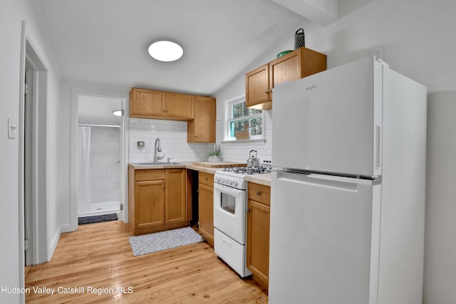 kitchen featuring decorative backsplash, a sink, light countertops, light wood finished floors, and white appliances