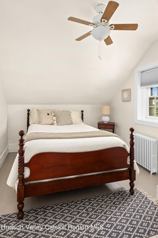 bedroom featuring hardwood / wood-style flooring, ceiling fan, radiator, and vaulted ceiling