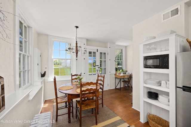 dining space with french doors, dark wood-type flooring, and an inviting chandelier