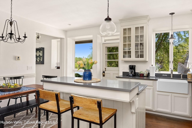 kitchen with dark wood-type flooring, sink, pendant lighting, white cabinets, and a chandelier