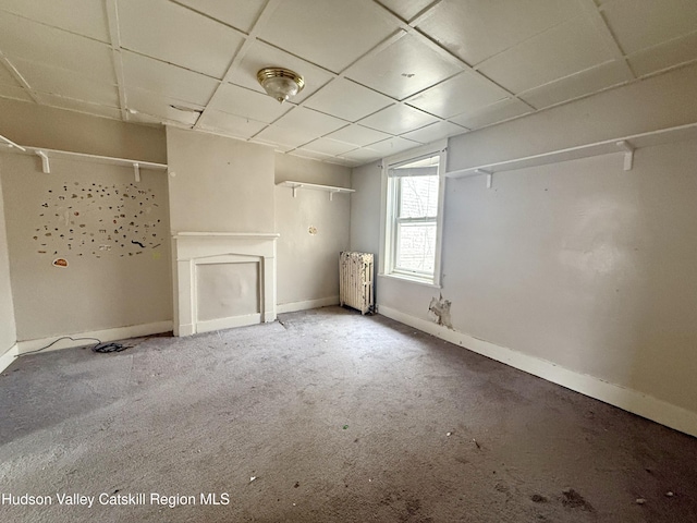 below grade area featuring a drop ceiling, carpet flooring, radiator heating unit, and baseboards