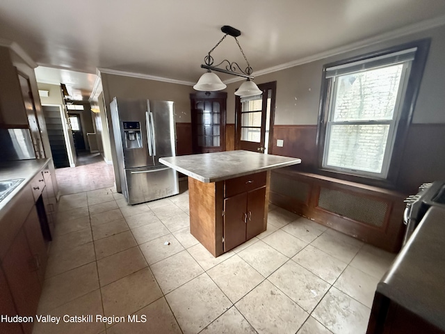 kitchen featuring a wainscoted wall, ornamental molding, a kitchen island, stainless steel fridge with ice dispenser, and hanging light fixtures