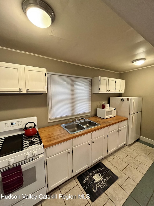 kitchen featuring white appliances, a sink, wood counters, baseboards, and white cabinets