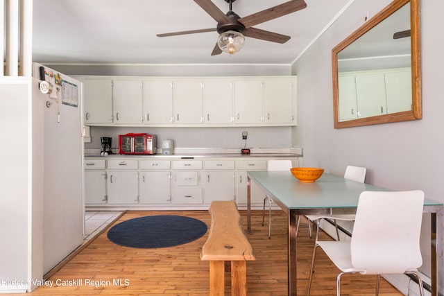 kitchen with light wood finished floors, ceiling fan, ornamental molding, light countertops, and white cabinetry