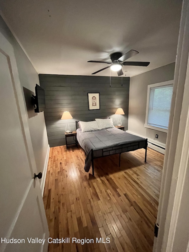 bedroom with an accent wall, light wood-type flooring, baseboards, and baseboard heating