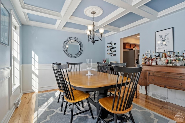 dining space featuring coffered ceiling, light wood-type flooring, beam ceiling, and a chandelier