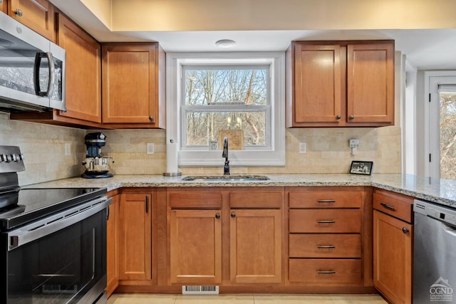 kitchen with appliances with stainless steel finishes, a sink, backsplash, and light stone countertops