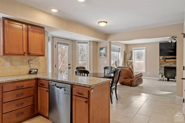 kitchen with stainless steel dishwasher, open floor plan, a peninsula, light carpet, and brown cabinetry