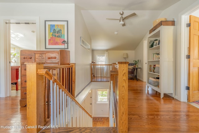 corridor with wood finished floors, a wealth of natural light, lofted ceiling, and an upstairs landing