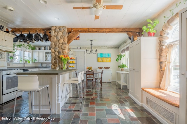 kitchen with a kitchen breakfast bar, dark countertops, visible vents, under cabinet range hood, and white gas range