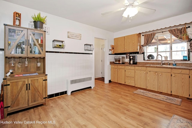 kitchen with radiator, ceiling fan, sink, tile walls, and light hardwood / wood-style floors