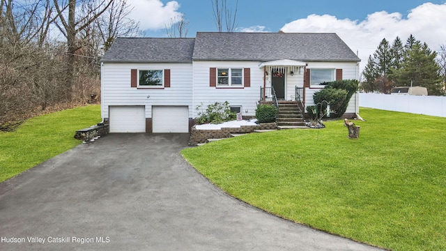 view of front of property featuring driveway, a garage, roof with shingles, fence, and a front yard