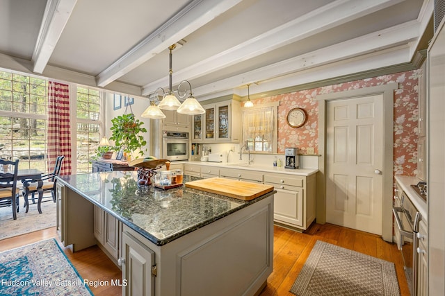 kitchen featuring light wood-type flooring, stainless steel appliances, pendant lighting, beamed ceiling, and a center island