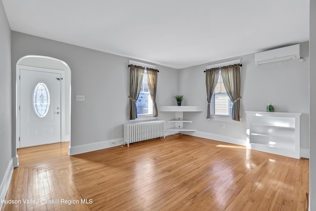 foyer with a wall mounted air conditioner, radiator heating unit, and hardwood / wood-style floors