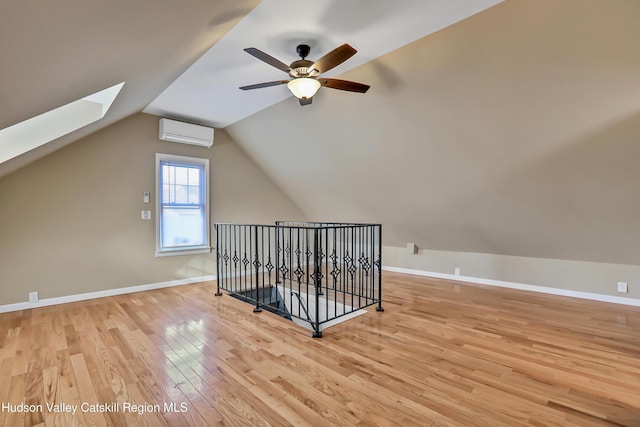 additional living space with light wood-type flooring, a wall unit AC, ceiling fan, and vaulted ceiling with skylight