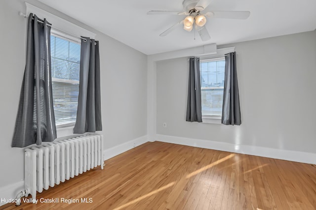 empty room featuring radiator, ceiling fan, plenty of natural light, and wood-type flooring