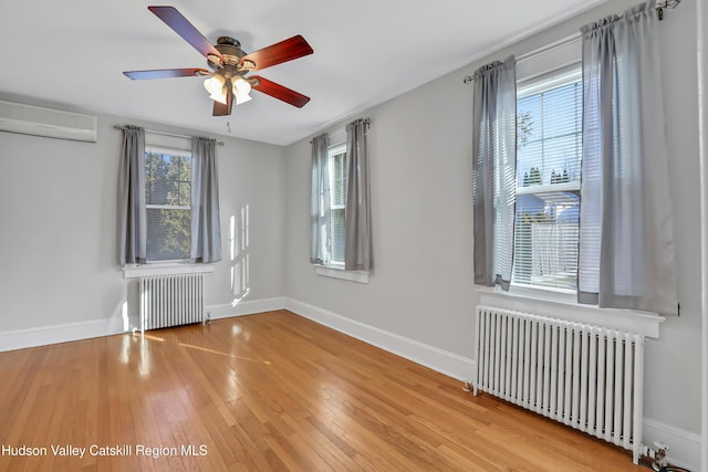 spare room featuring a wall mounted air conditioner, ceiling fan, radiator heating unit, and hardwood / wood-style floors