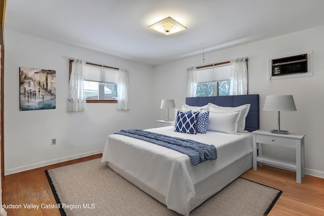 bedroom featuring an AC wall unit, multiple windows, and wood-type flooring