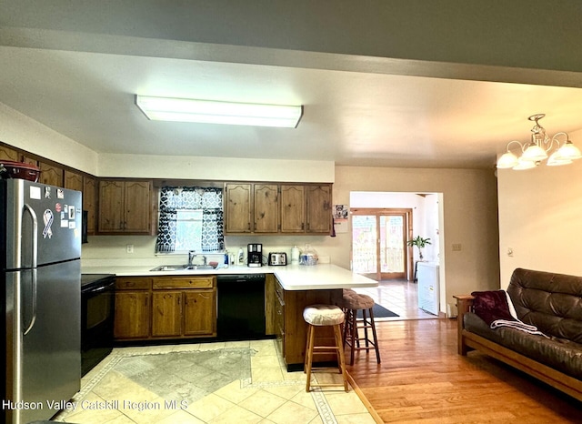 kitchen with kitchen peninsula, a kitchen breakfast bar, sink, black appliances, and hanging light fixtures