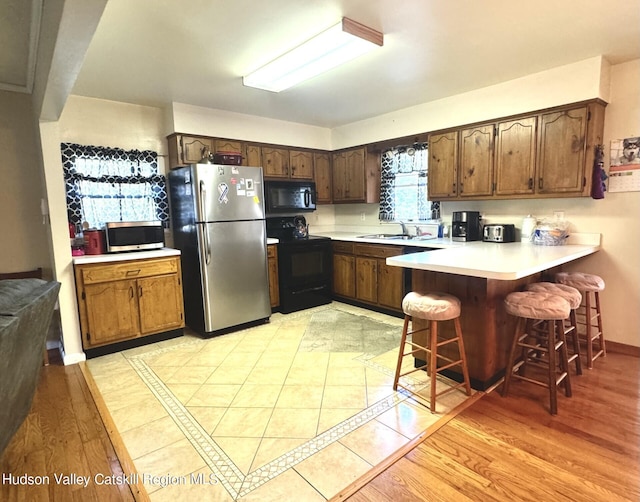 kitchen with sink, kitchen peninsula, light hardwood / wood-style floors, a breakfast bar, and black appliances