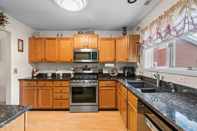 kitchen with stainless steel appliances, light hardwood / wood-style floors, sink, and dark stone countertops