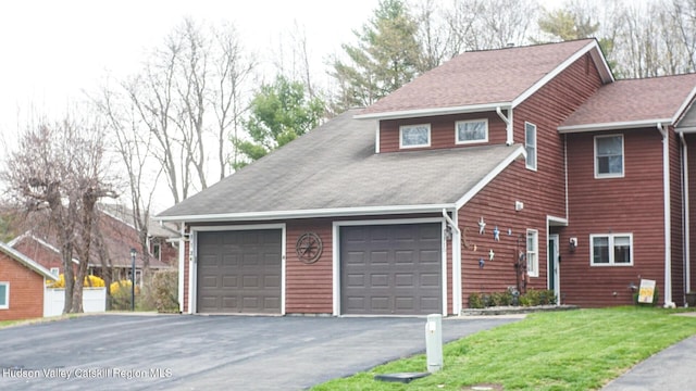 exterior space with an attached garage, driveway, roof with shingles, and a front lawn