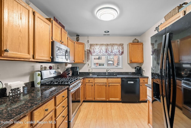 kitchen with sink, light hardwood / wood-style flooring, black appliances, and dark stone counters