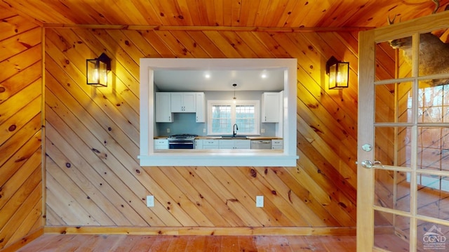 unfurnished living room featuring a sink, wooden walls, wooden ceiling, and wood finished floors