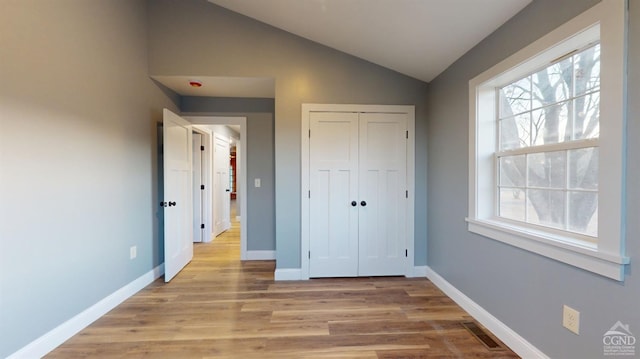 unfurnished bedroom with vaulted ceiling, light wood finished floors, multiple windows, and baseboards