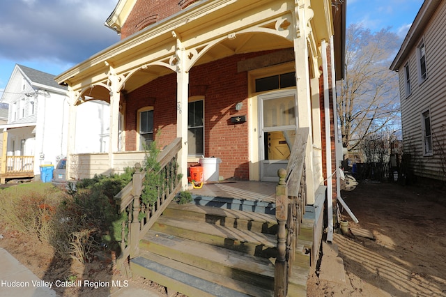 view of exterior entry with brick siding and a porch