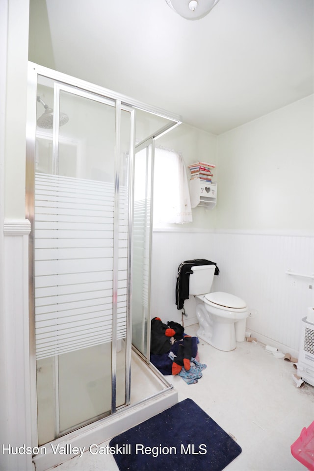 full bath with a shower stall, toilet, and a wainscoted wall