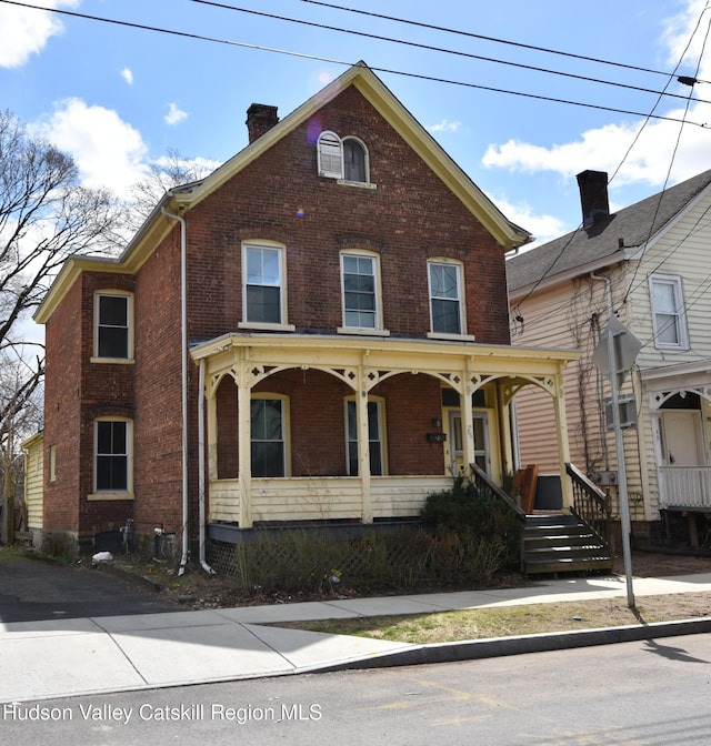 view of front of property featuring brick siding, a porch, and a chimney